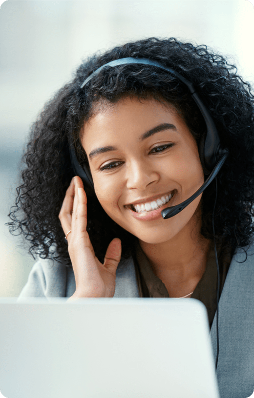 A smiling woman looking at her laptop wearing headphones